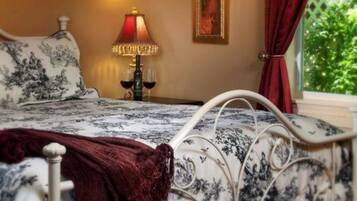 A bed with a floral bedspread, a red throw blanket, and a bedside table with a lamp and wine glasses.
