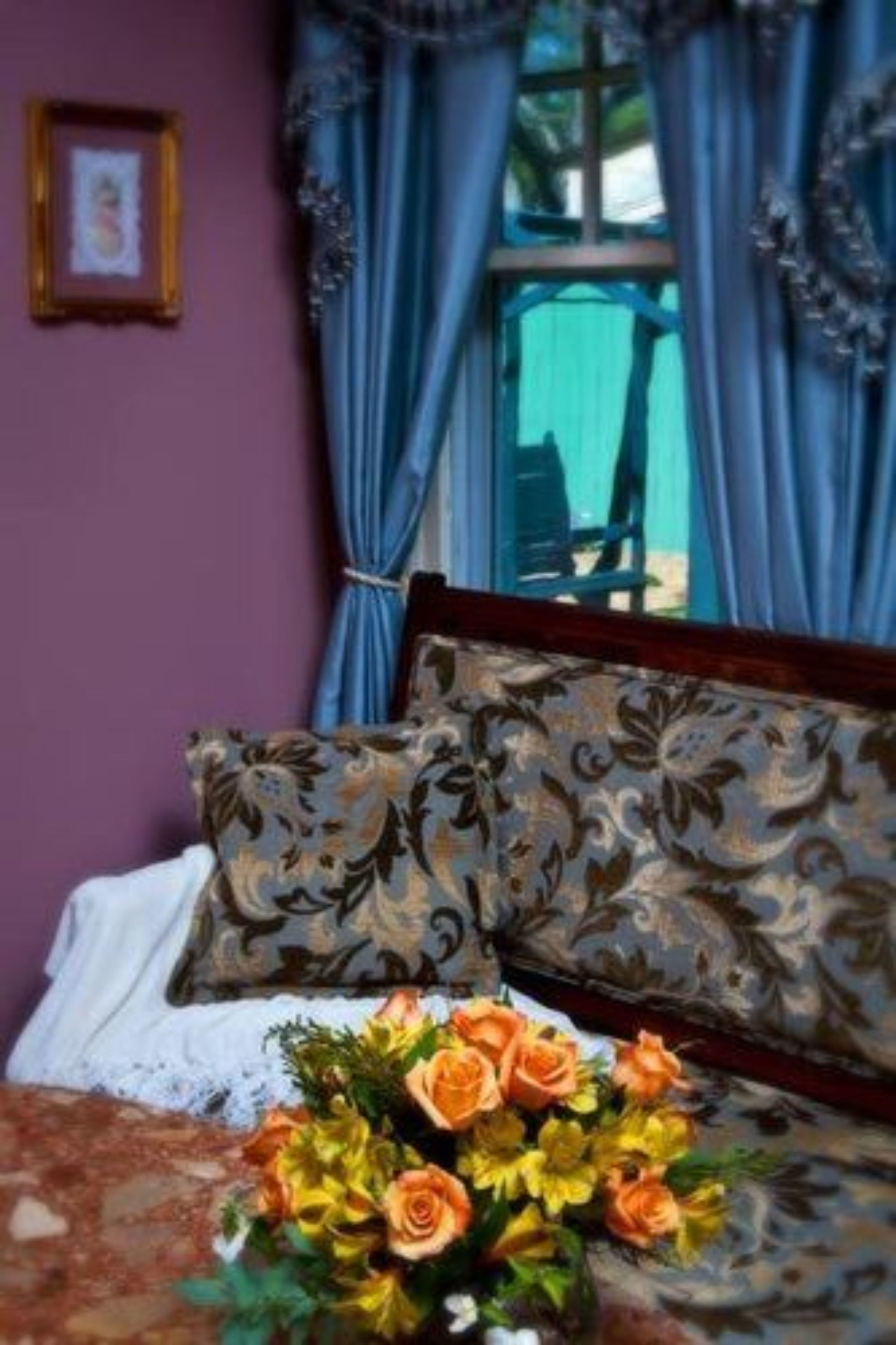 A bedroom with a bed, floral pillows, and a bouquet of flowers.