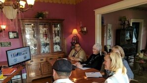 A group of people seated around a wooden table in a room with a pink wall and a chandelier. - The Carriage House B&B (Jefferson)