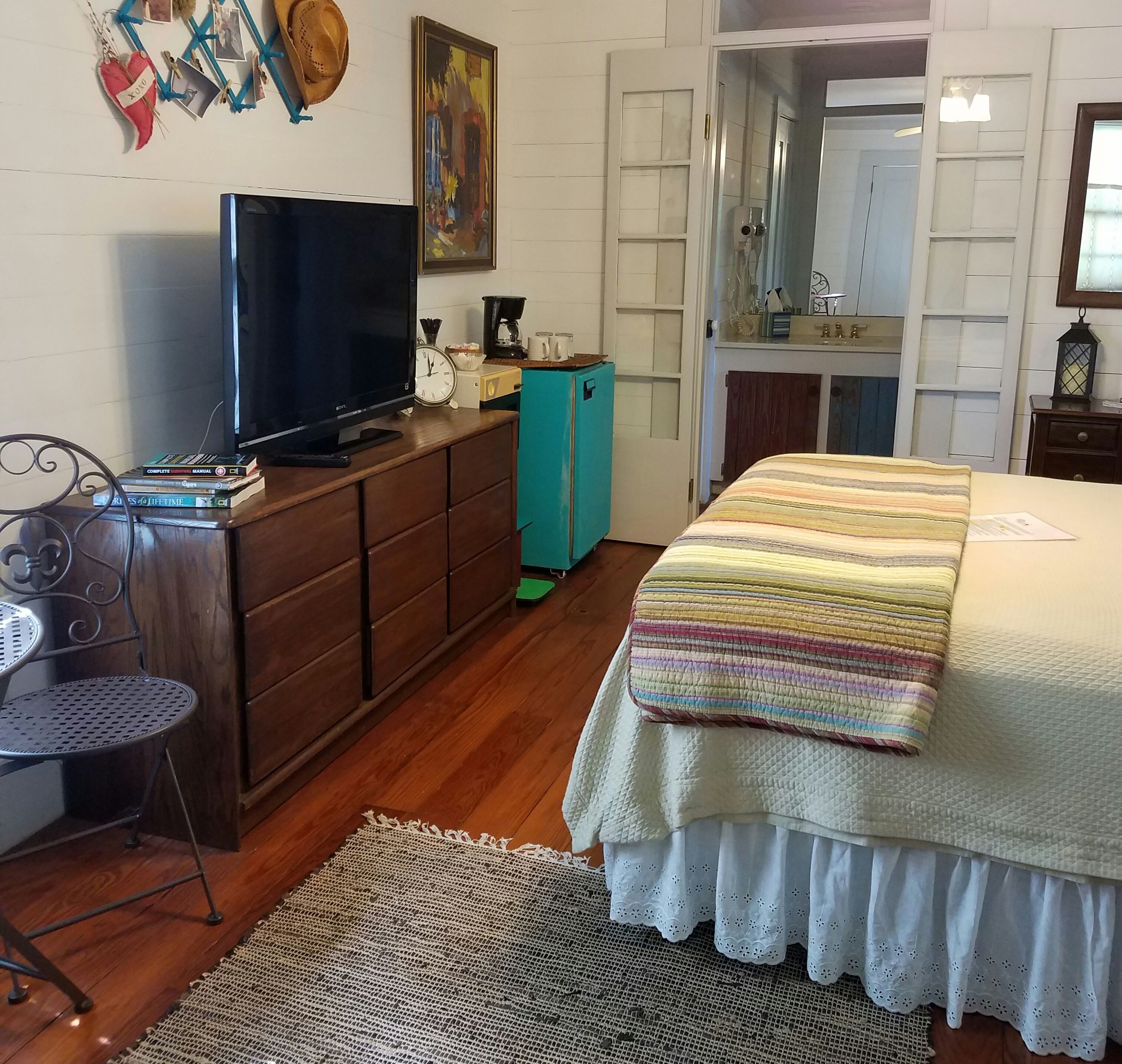 A bedroom with a bed, a TV on a dresser, a coffee maker, and a door leading to another room.