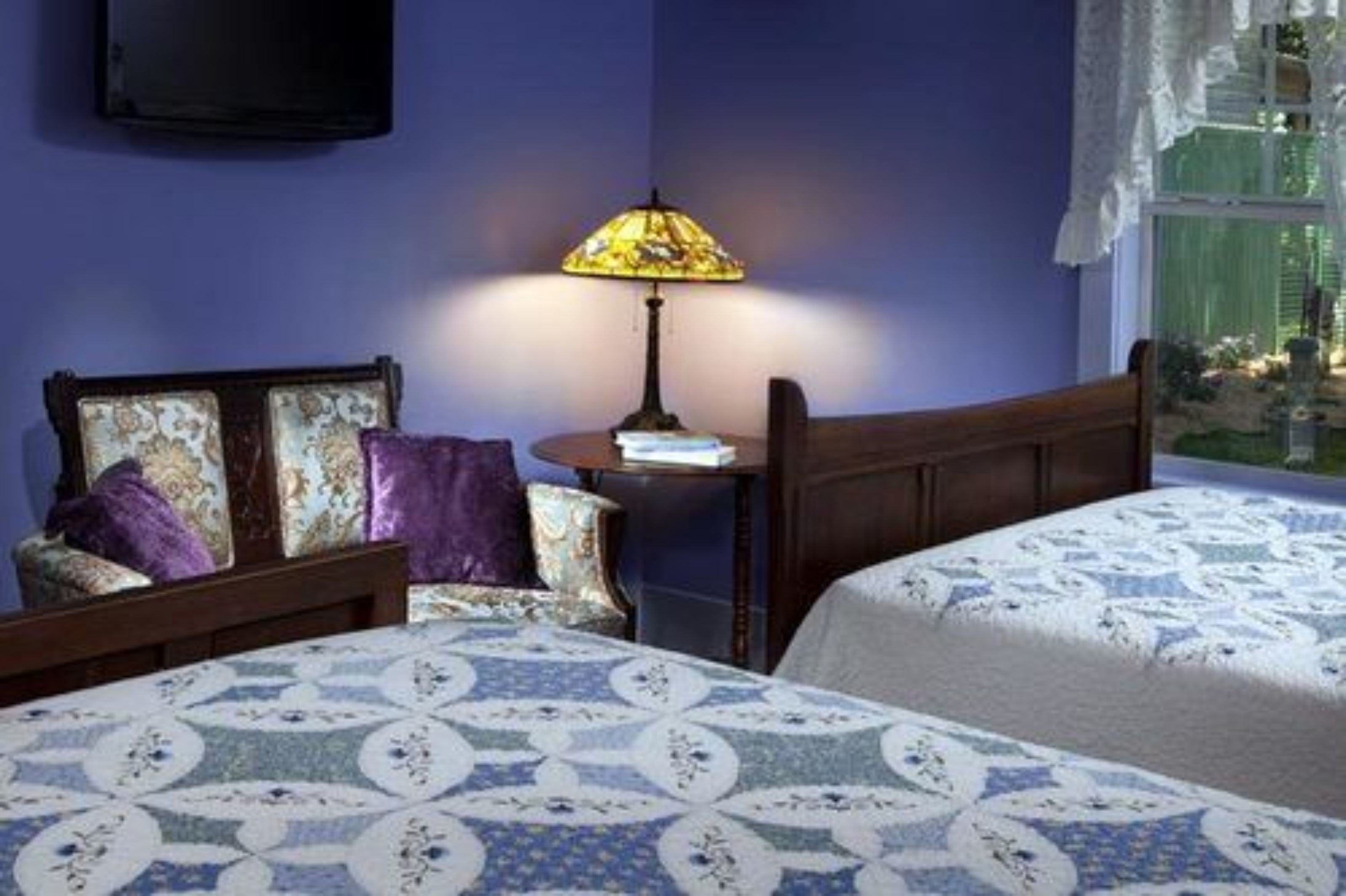 A bedroom with a bed, a nightstand, a lamp, and a window with a view.
