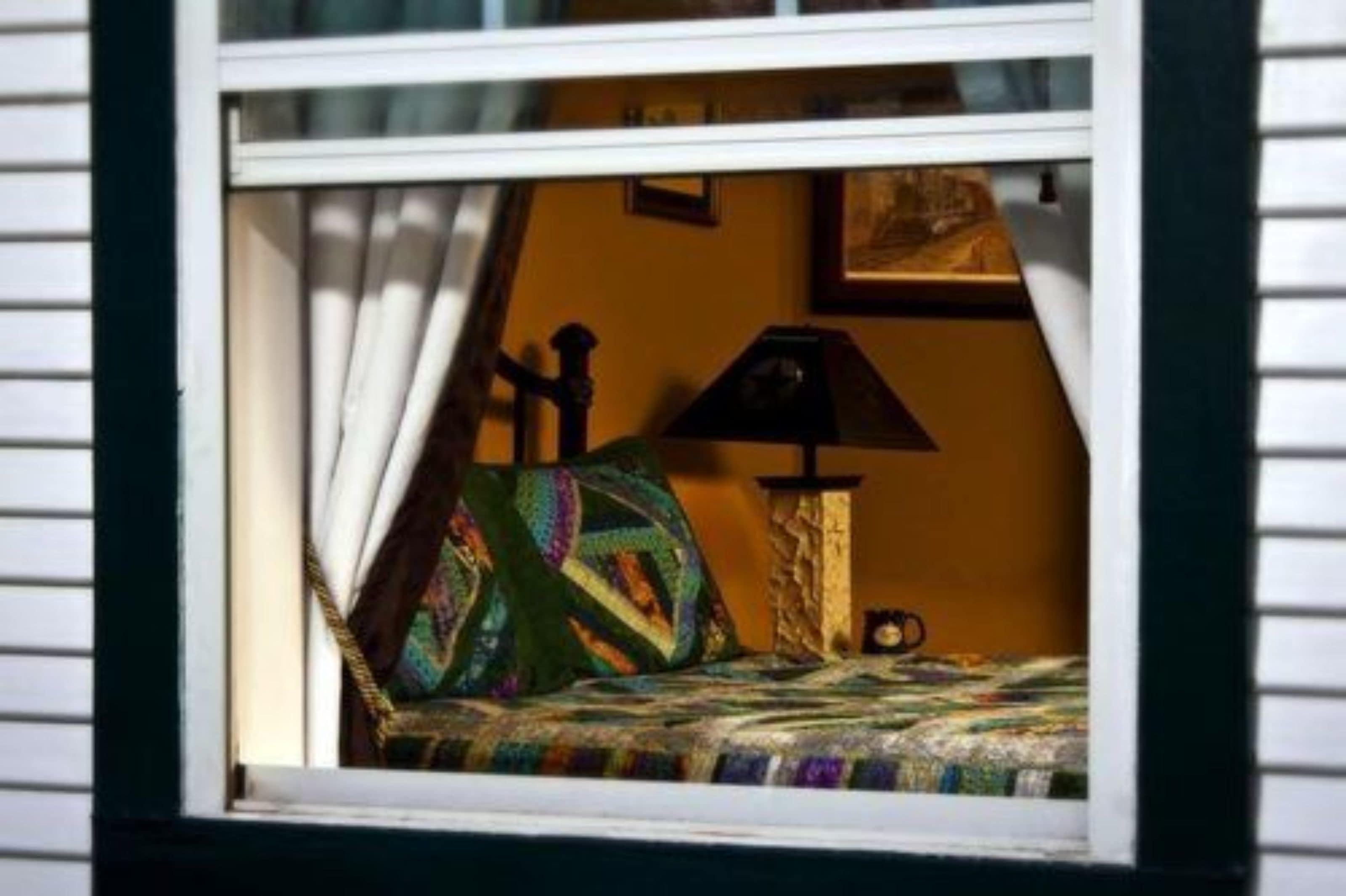Vista desde la ventana de una habitación con una cama, una lámpara y una mesita.