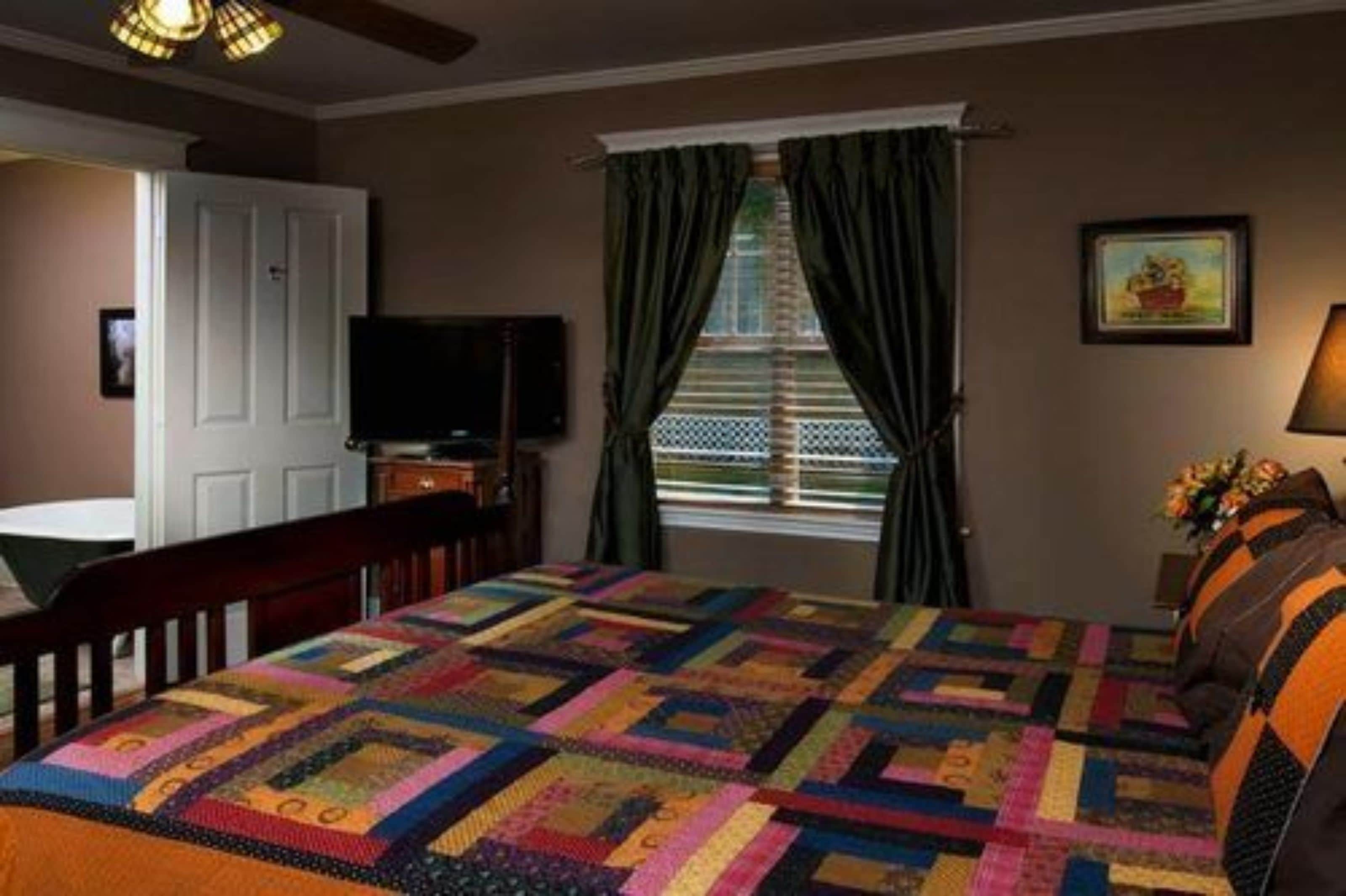 A bedroom with a large bed, a television, a window with curtains, and a painting on the wall.