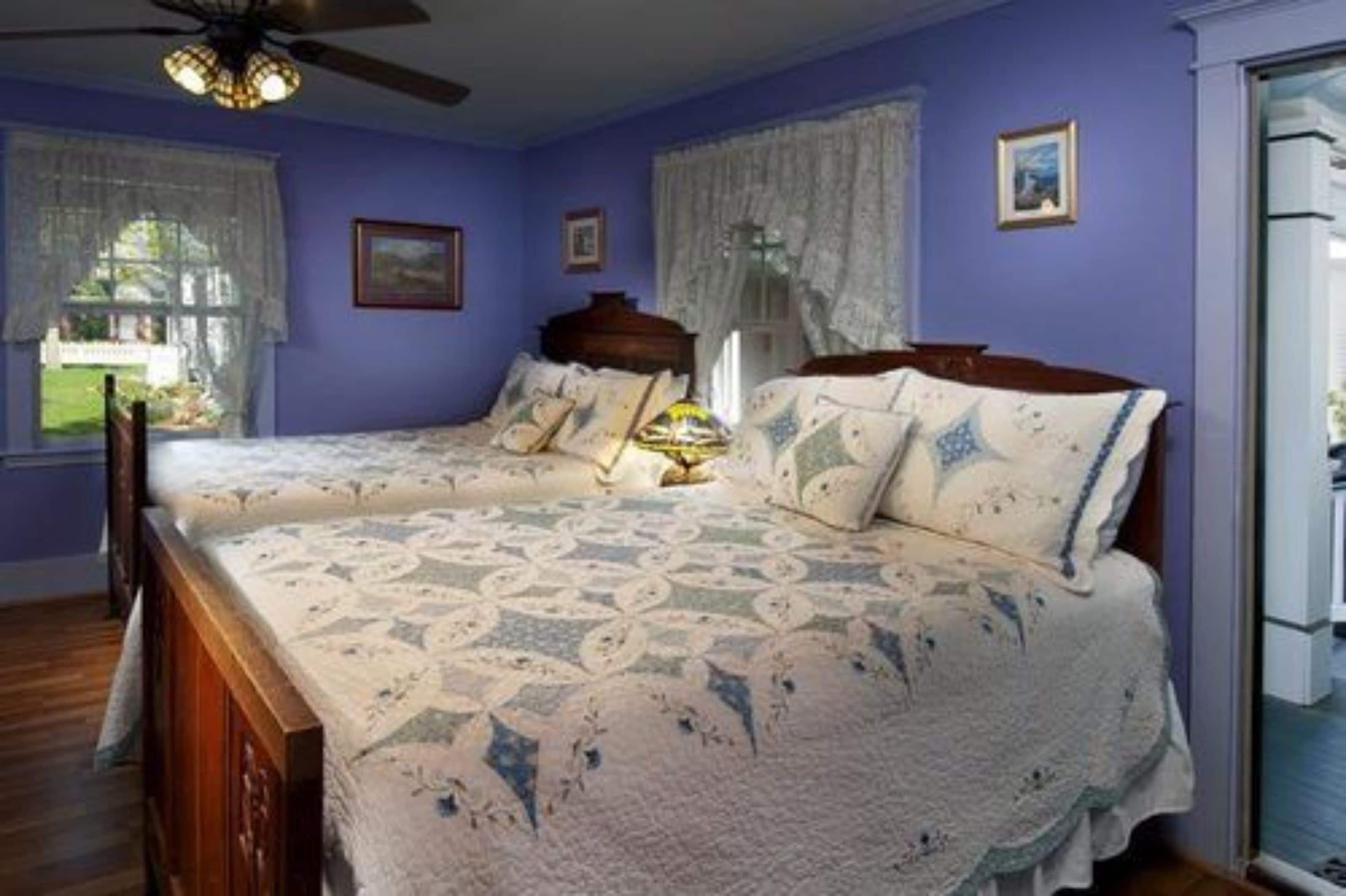 Een slaapkamer met twee bedden, een plafondventilator en een raam met kantgordijnen.