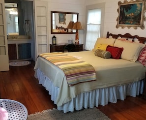 Quarto com uma cama grande, cabeceira de madeira, espelho, mesa de cabeceira, abajur e um quadro na parede.