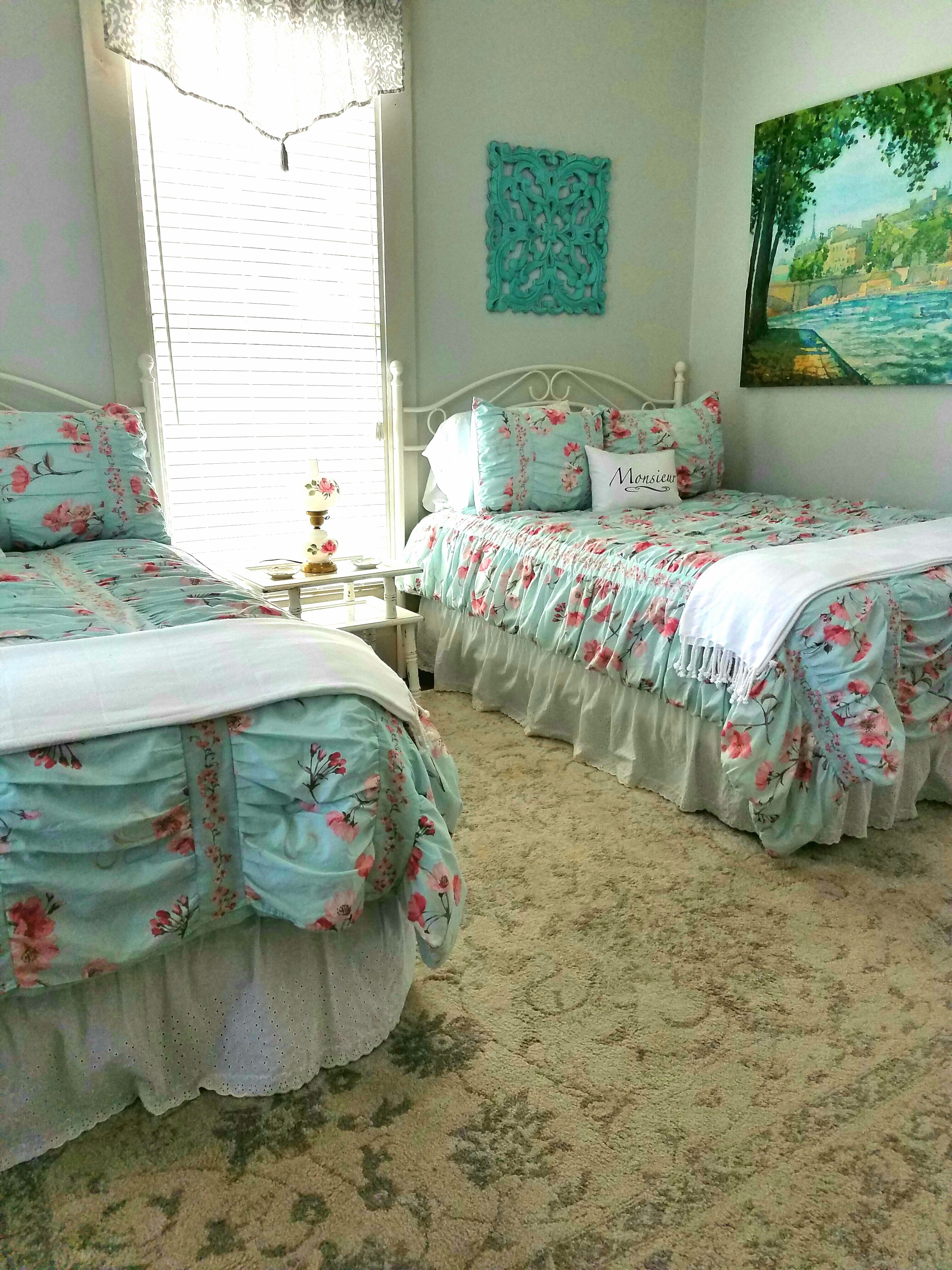 A bedroom with two beds, a window with blinds, a wall decoration, and a painting.