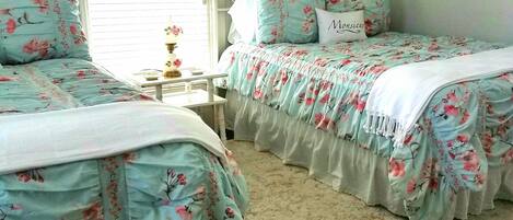 A bedroom with two beds, a window with blinds, a wall decoration, and a painting.