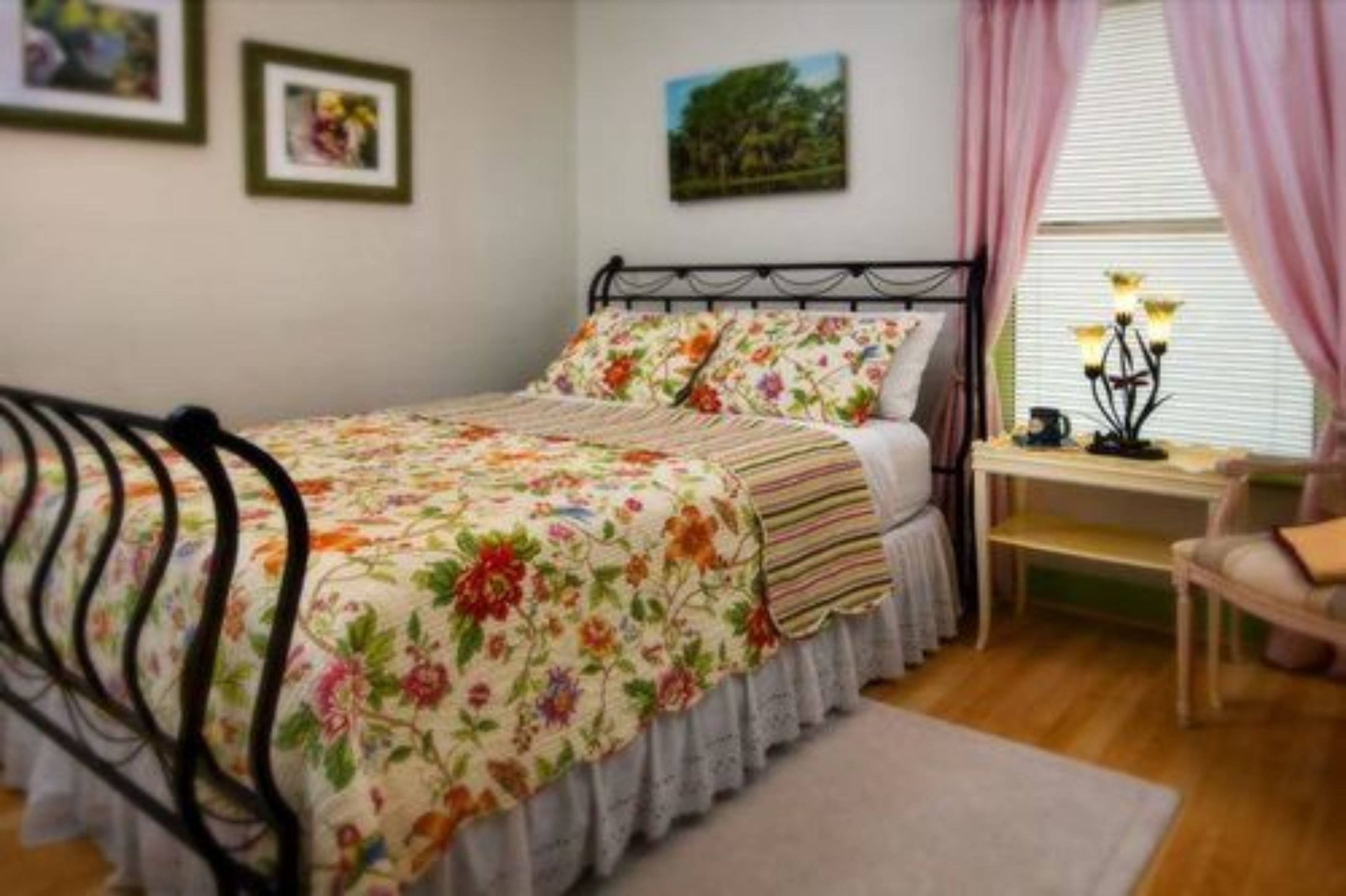 A bedroom with a floral bedspread, a bedside table with a lamp, and a chair.