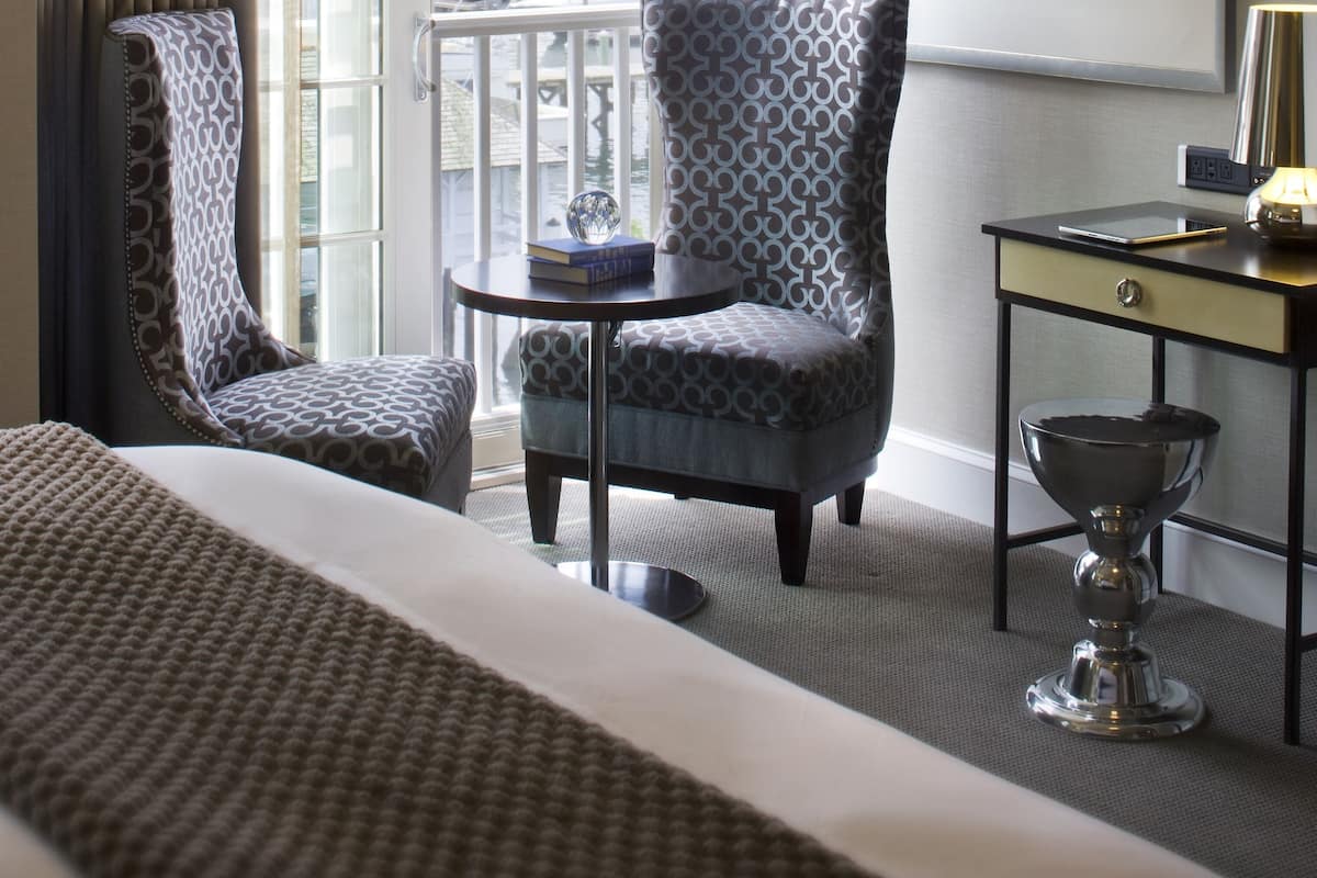 A hotel room with a large bed, a chair, a small table, a desk, and a view of the marina.