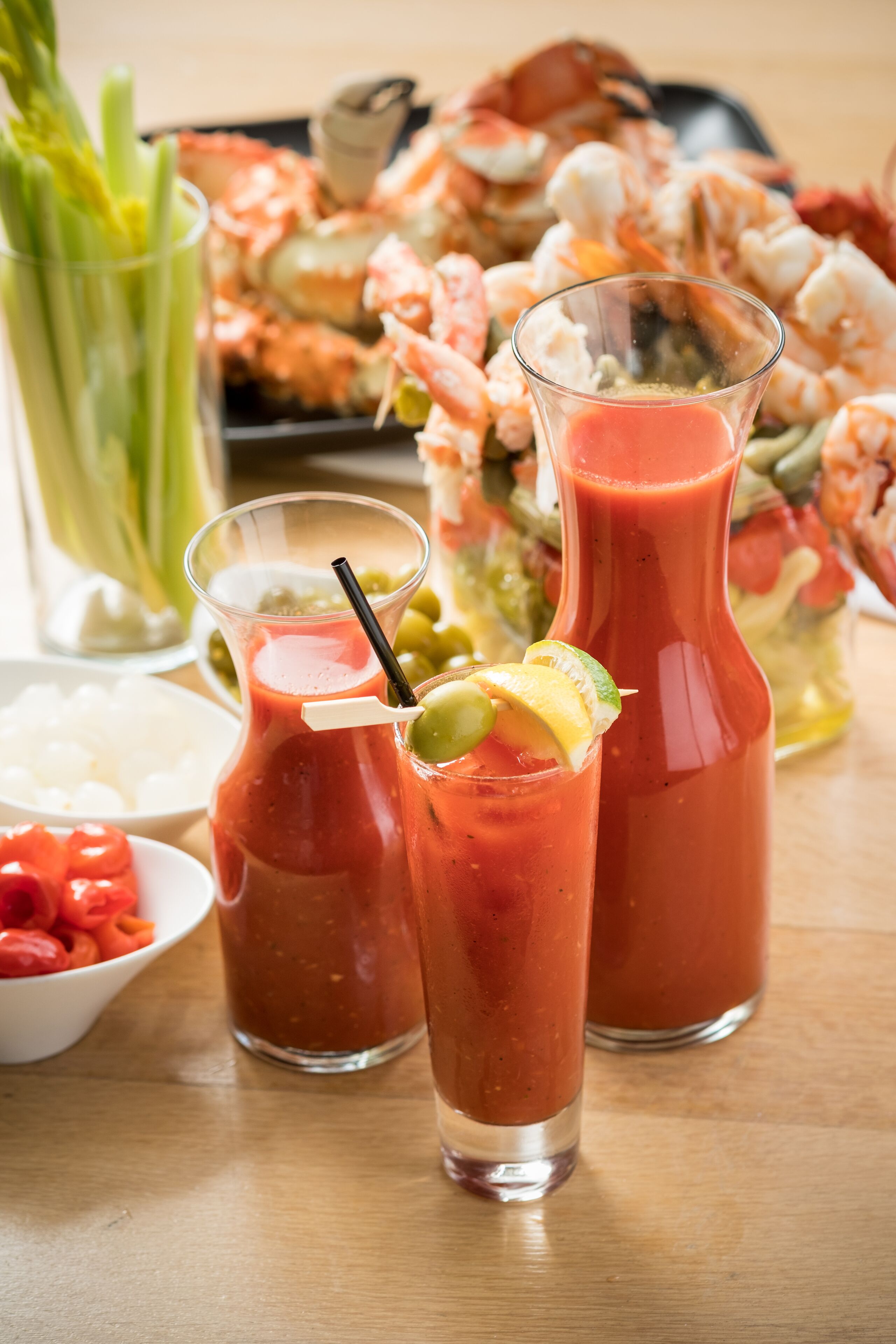 Una mesa con dos vasos de Bloody Mary, una jarra de Bloody Mary y un bol de camarones.