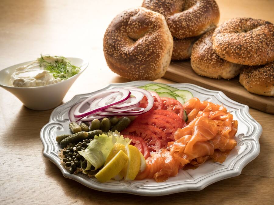 A plate of smoked salmon, vegetables, and bagels on a table.