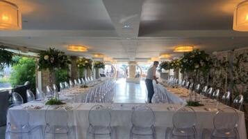 A long dining table set with chairs, centered with a person standing, and surrounded by floral arrangements.