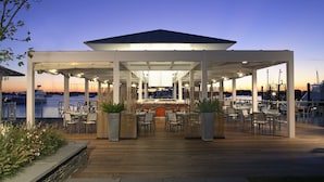 A covered outdoor dining area with tables and chairs, overlooking a marina with boats. - Forty 1 North (Newport)