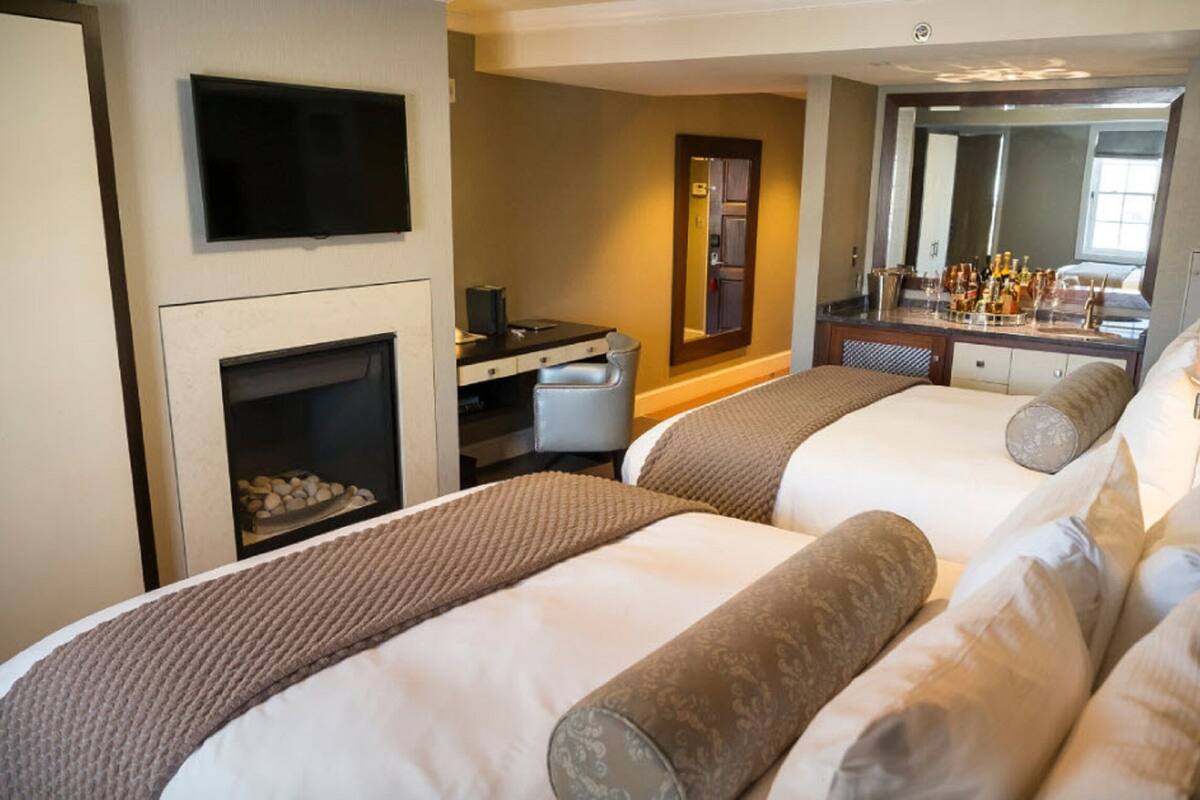 A hotel room with two beds, a TV, a desk, a mirror, and a minibar.