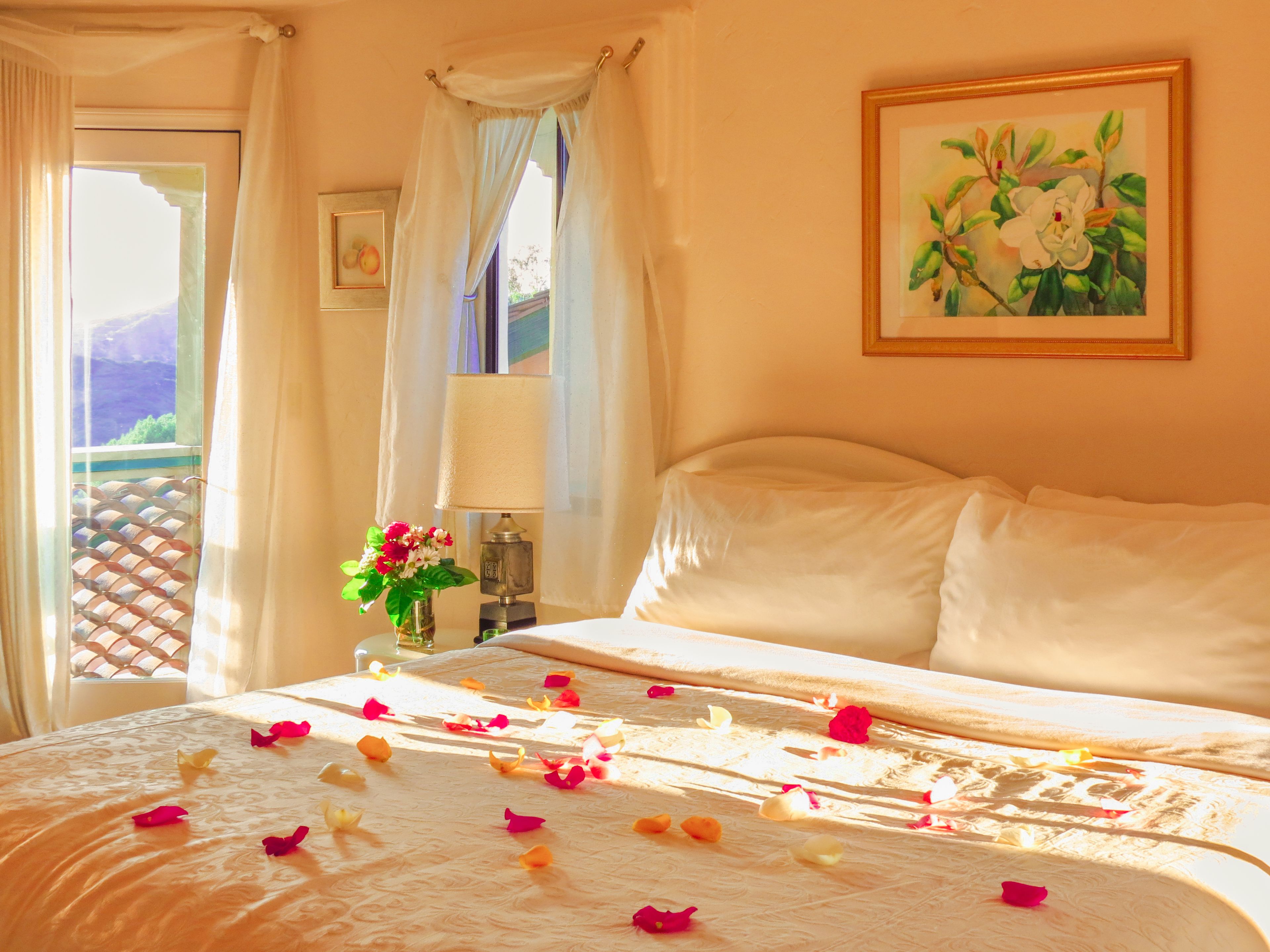 A hotel room with a bed, a nightstand, a lamp, a window with curtains, and a painting on the wall.