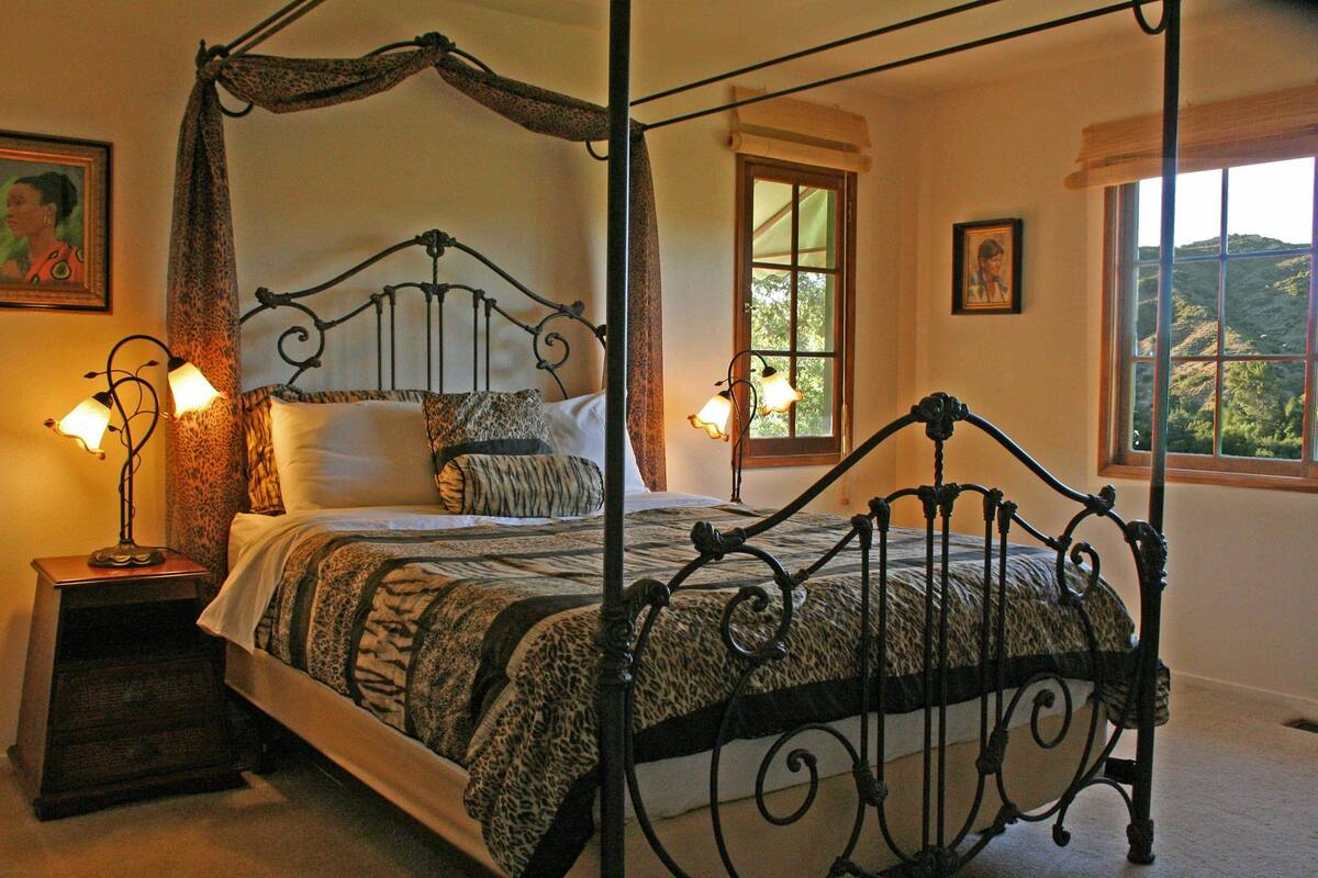 A four-poster bed with a canopy, two bedside lamps, and a view of the outdoors through a window.