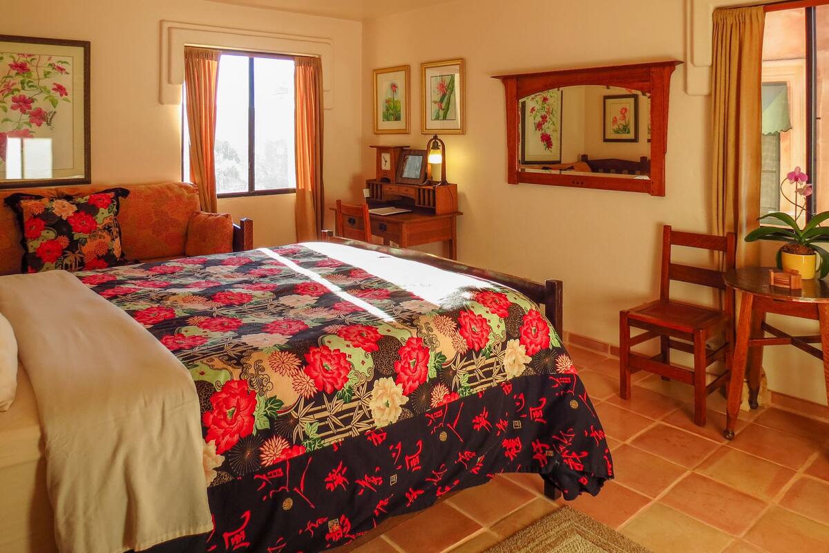 A bedroom with a large bed, a desk, a chair, and a window with curtains.