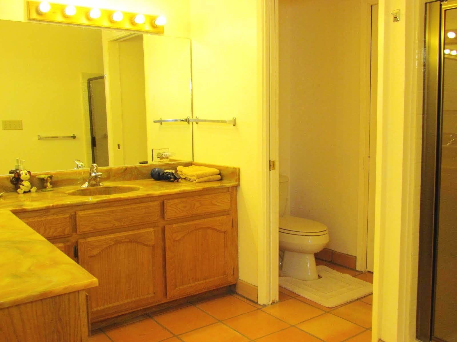 A bathroom with a wooden vanity, a sink, a mirror with lights, a towel rack, and a toilet.
