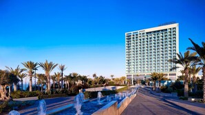 A hotel with a modern facade, a water feature in the foreground, and palm trees lining the walkway. - Le Méridien Oran Hotel & Convention Centre (Oran)
