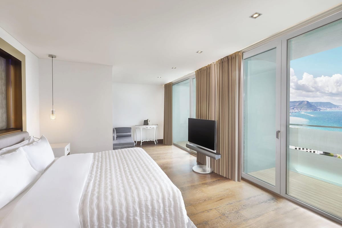 Une chambre d’hôtel moderne dotée d’un grand lit, d’une télévision à écran plat, d’une petite table et d’un balcon offrant une vue sur la mer.