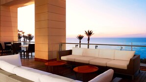 A modern outdoor lounge area with a sofa, round tables, and a view of the ocean at sunset. - Le Méridien Oran Hotel & Convention Centre (Oran)