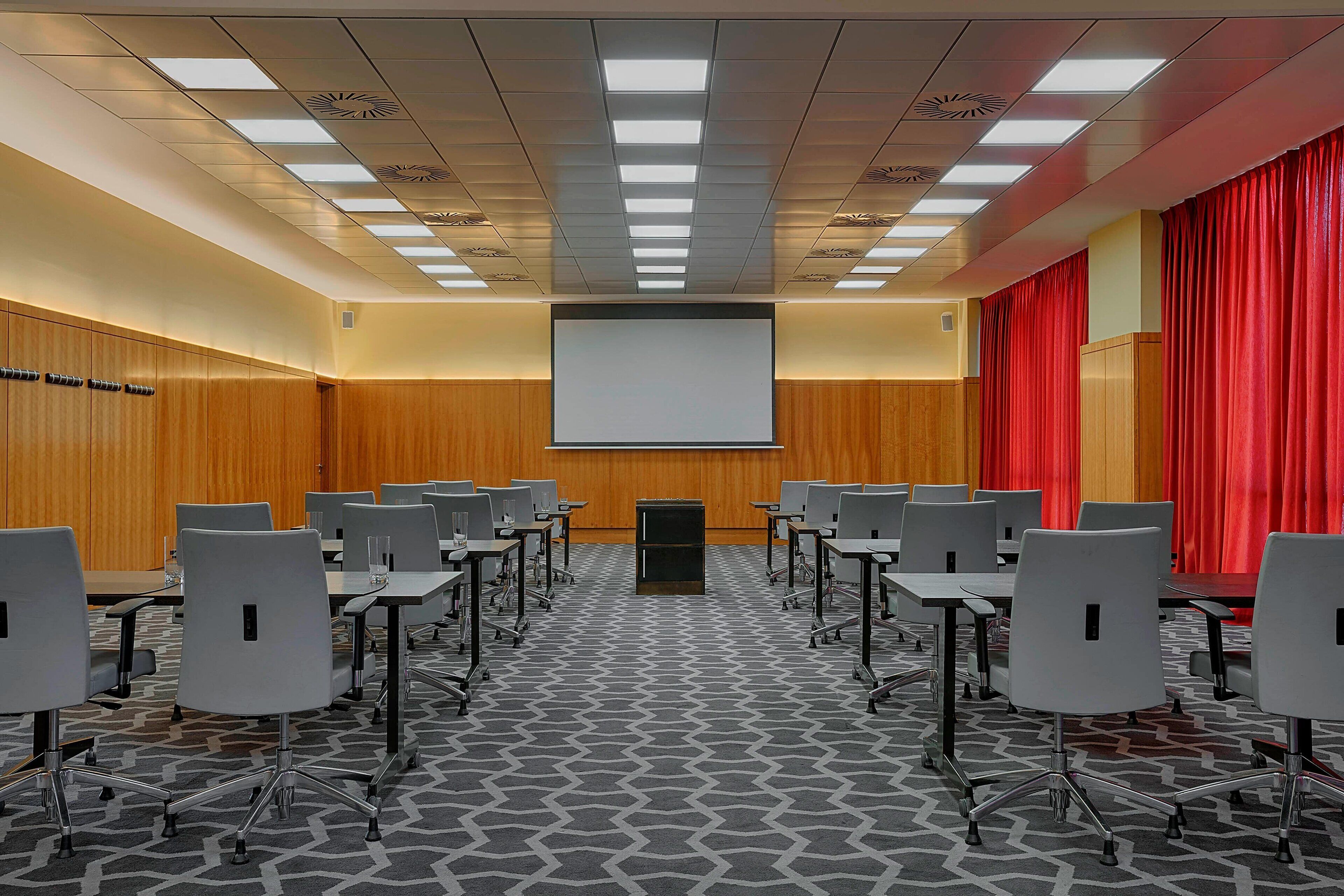 A conference room with a large screen, rows of chairs, and a patterned carpet.