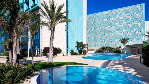 A modern hotel with a large infinity pool, palm trees, and a blue patterned wall. - Le Méridien Oran Hotel & Convention Centre (Oran)