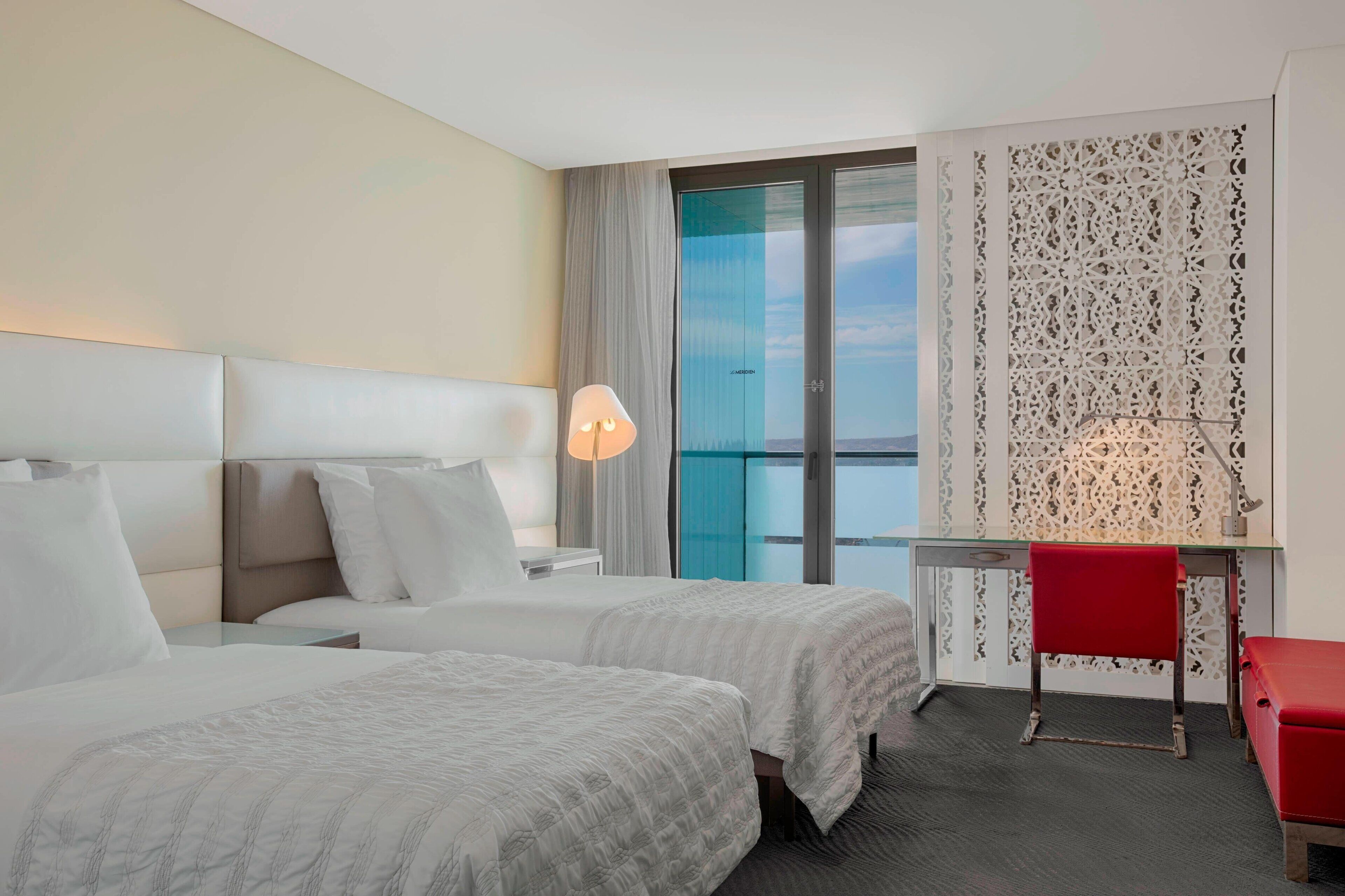 A hotel room with two beds, a desk, a chair, and a large window with a view.