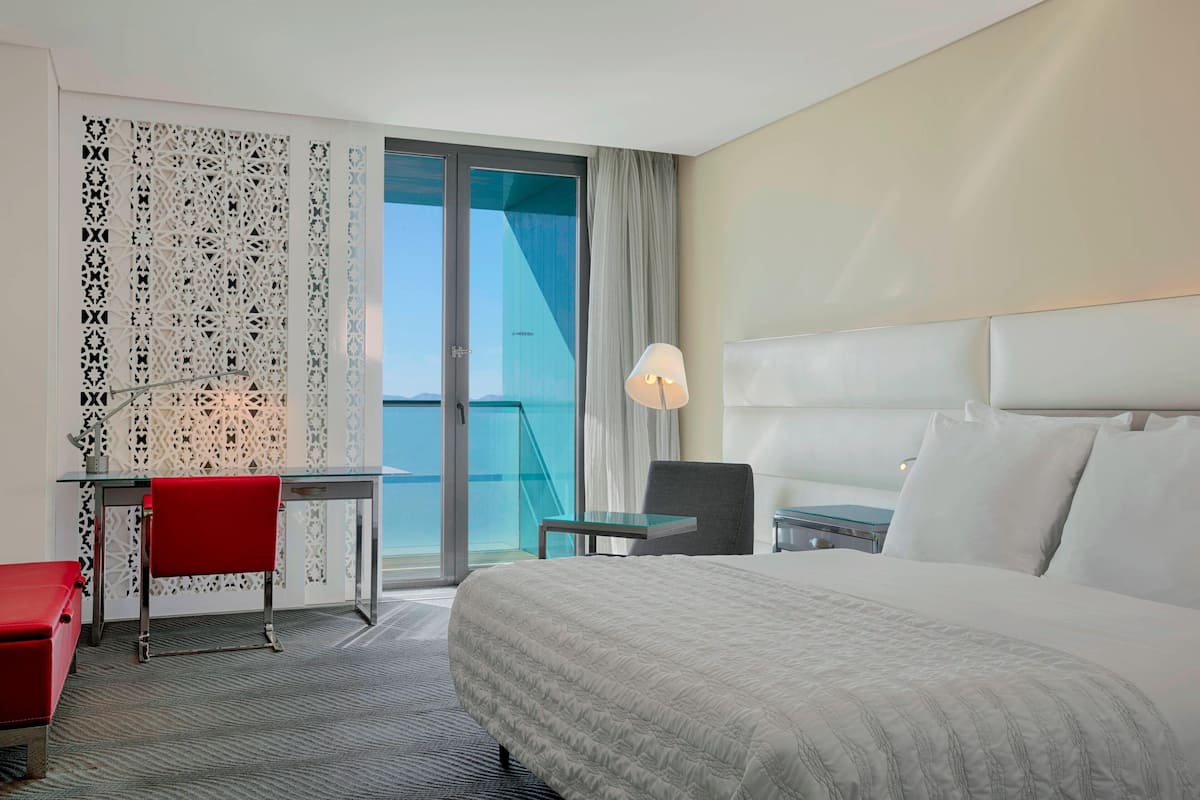 Une chambre d’hôtel équipée d’un lit, d’un bureau, d’une chaise, d’une lampe et offrant une vue sur l’extérieur.