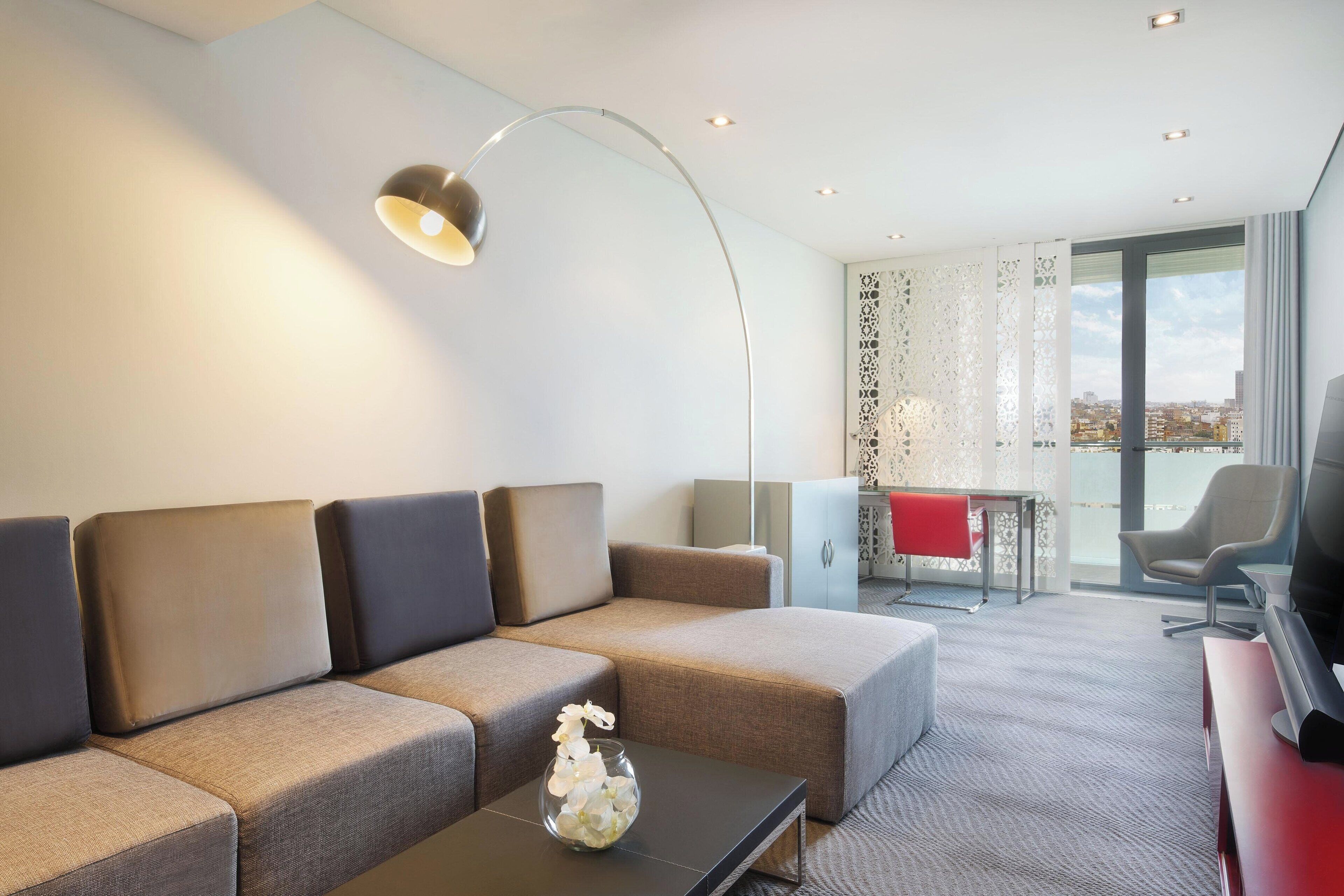 En moderne stue med en hjørnesofa, et glasbord og et fjernsyn.