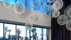 A modern hotel room with a large window, a white sofa, red chairs, and a unique ceiling light fixture. - Le Méridien Oran Hotel & Convention Centre (Oran)