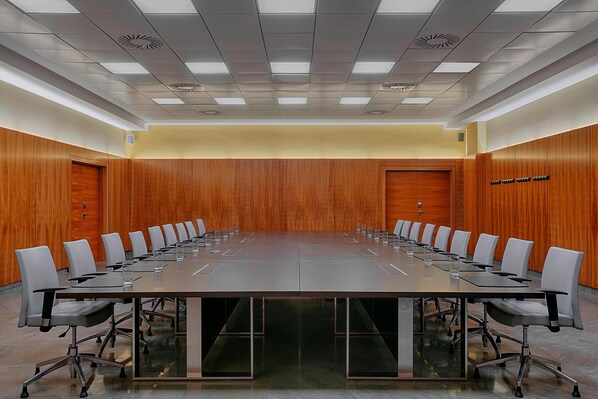 Un salón de conferencias con una mesa larga, sillas y una pared de madera.