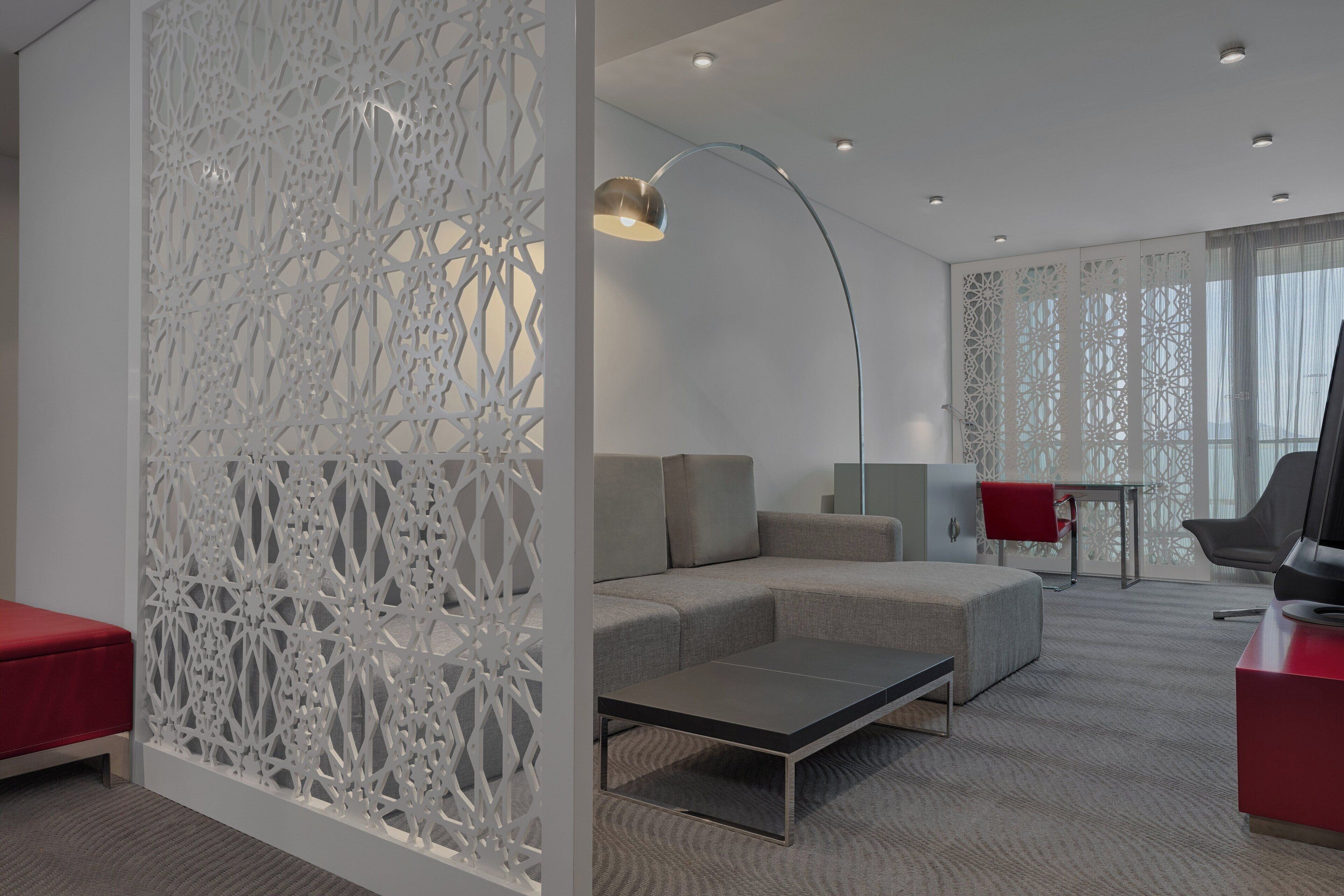 A modern living room with a sectional sofa, a coffee table, a red chair, a TV, and a decorative white partition.