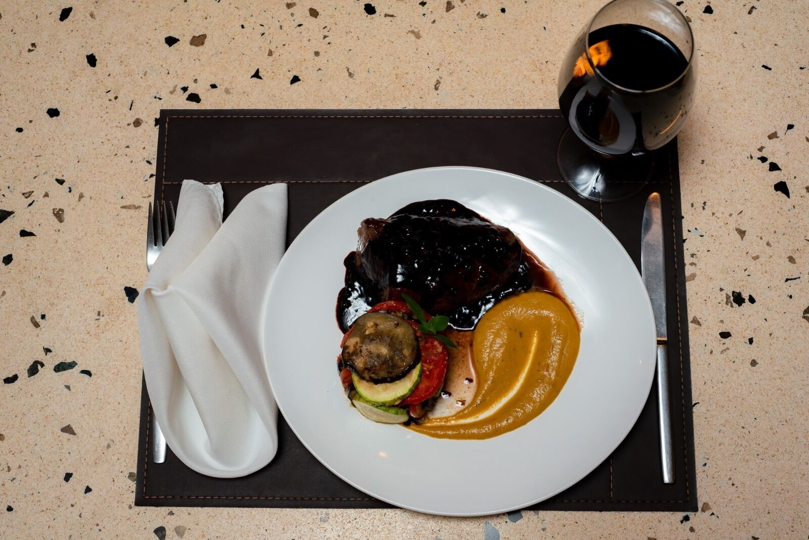 A plate of food with a dark sauce, a slice of meat, and a side of mashed potatoes on a speckled countertop.