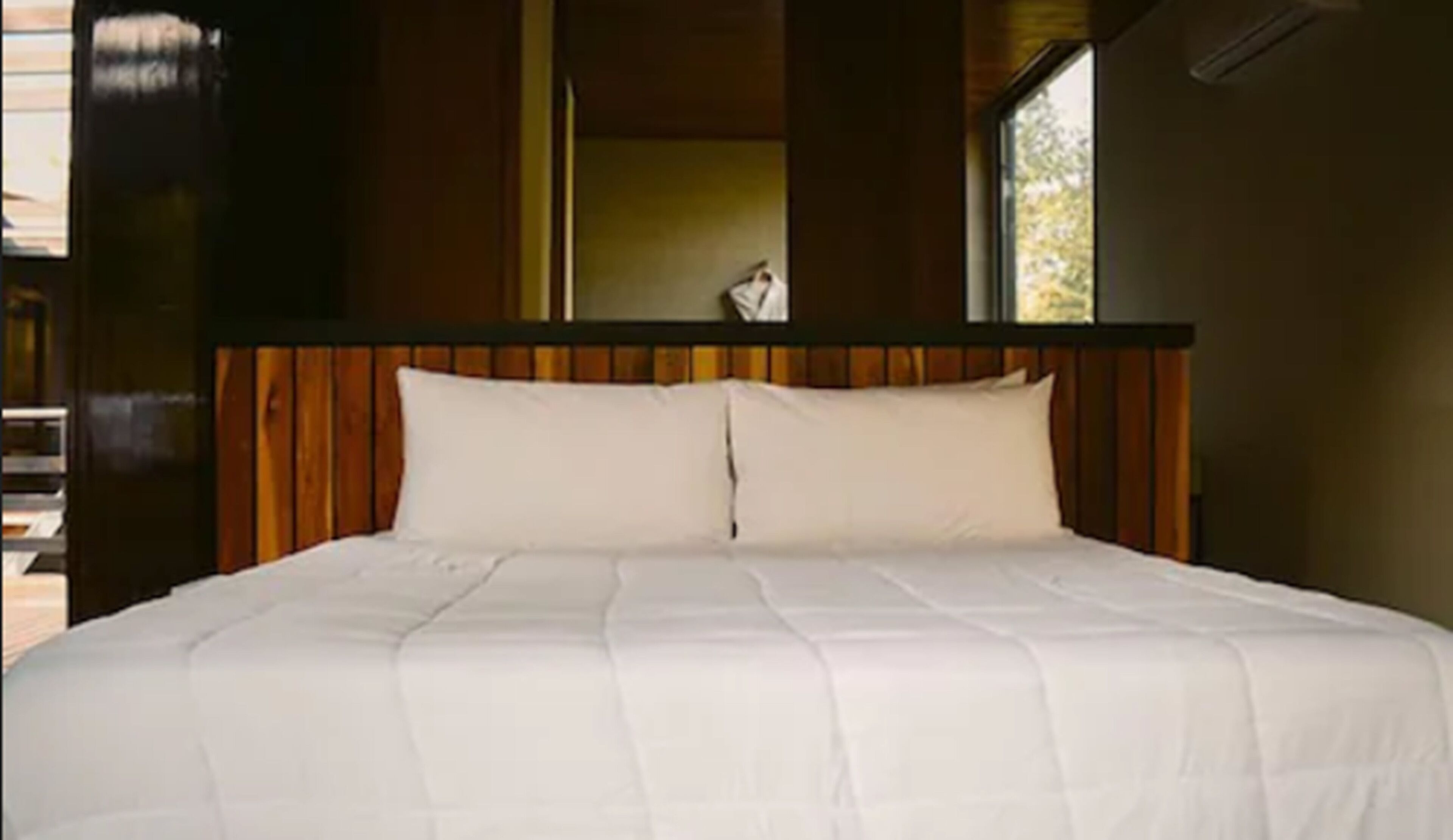 A bed with a wooden headboard and white bedding in a room with a window.