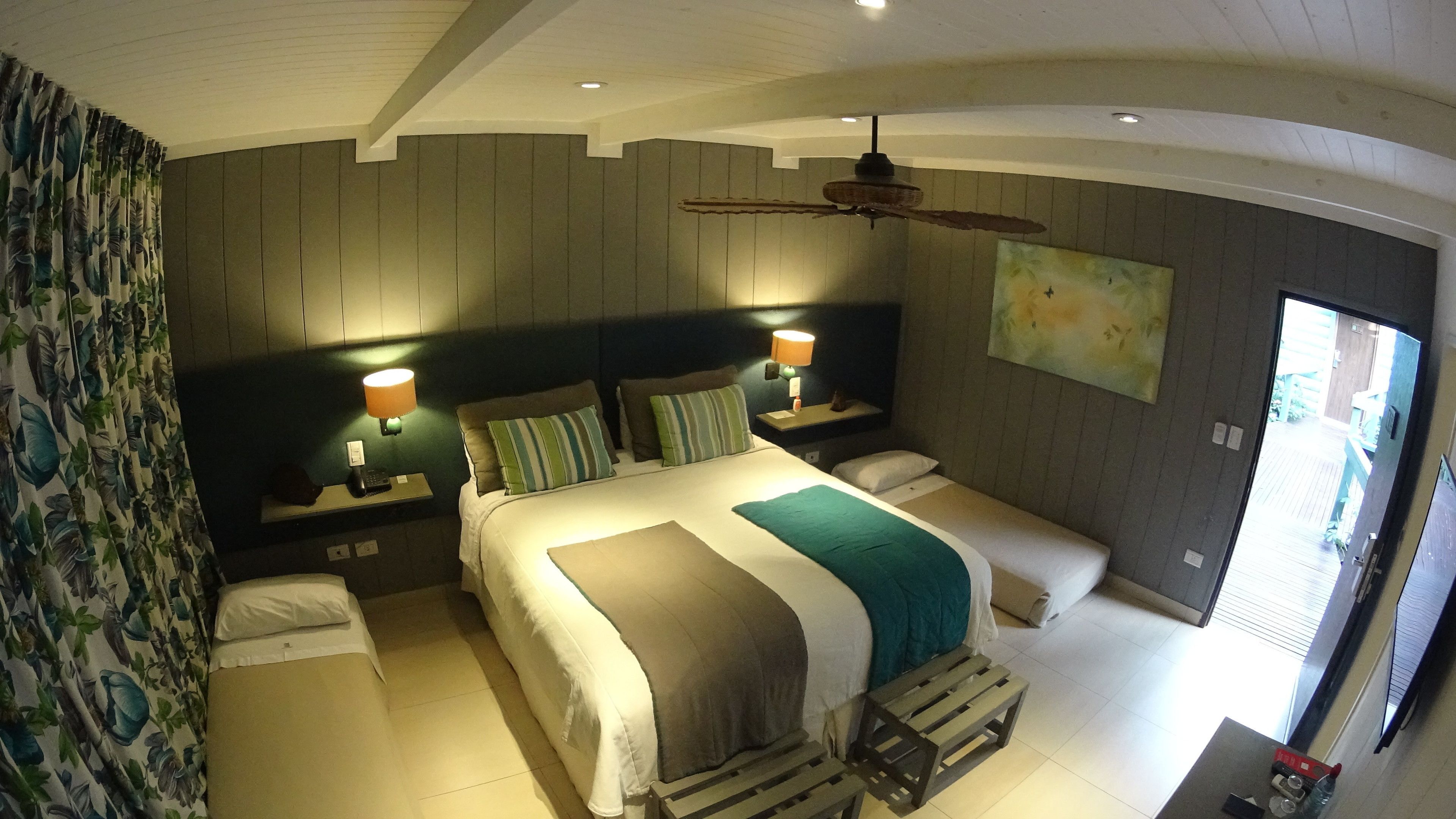 A bedroom with a large bed, two bedside tables with lamps, a ceiling fan, and a painting on the wall.