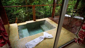 Un jacuzzi con paredes de vidrio y suelo de baldosas, rodeado de abundante follaje.