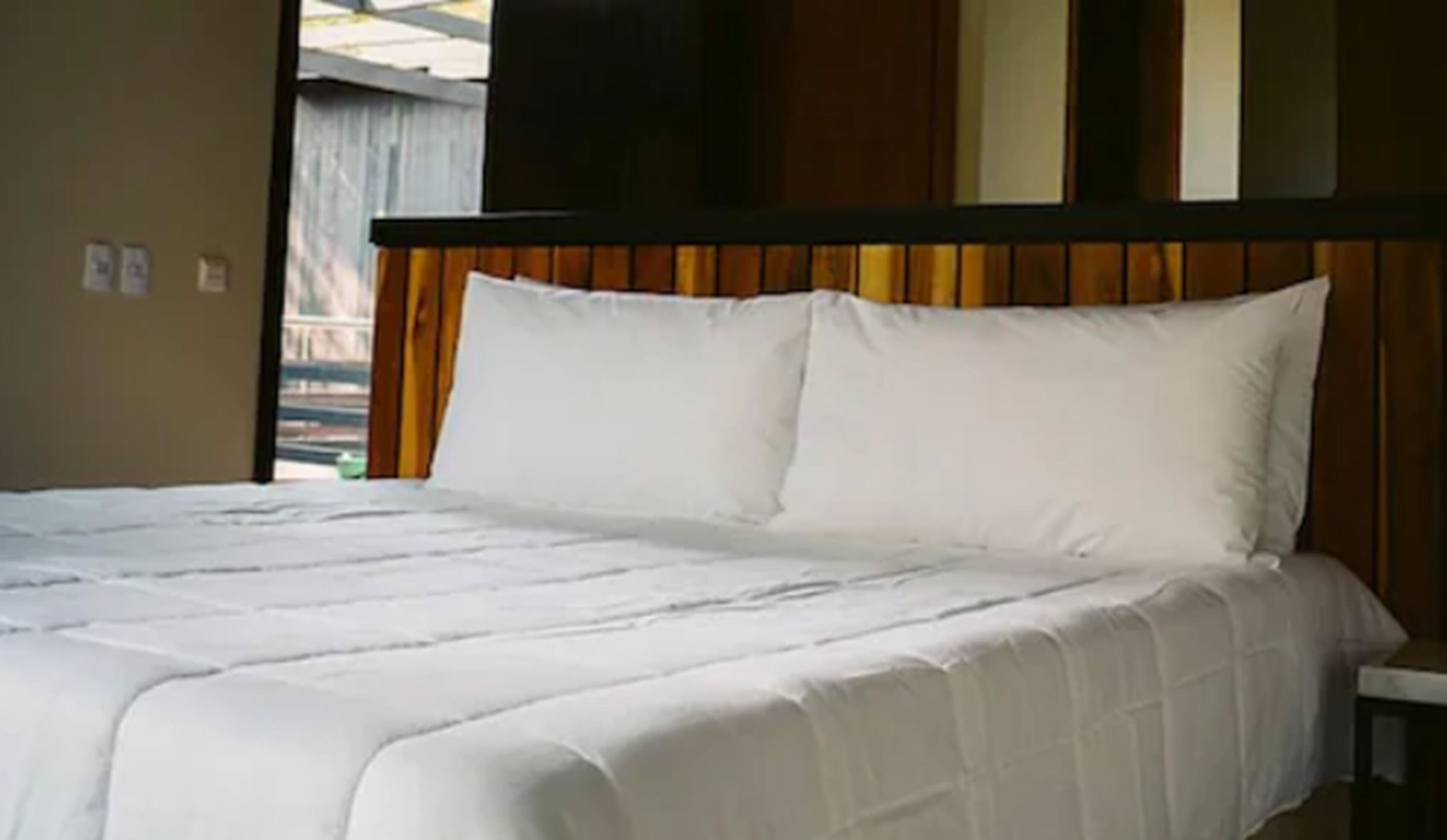 A bed with white bedding in a room with wooden headboard and beige walls.