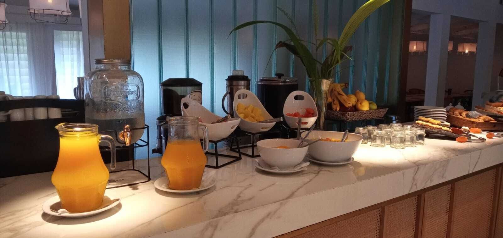 Een ontbijtbuffet met sinaasappelsap, kommen met eten en diverse soorten fruit.