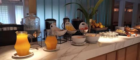 Een ontbijtbuffet met sinaasappelsap, kommen met eten en diverse soorten fruit.