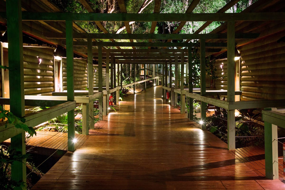 A wooden pathway with a covered structure, surrounded by greenery.