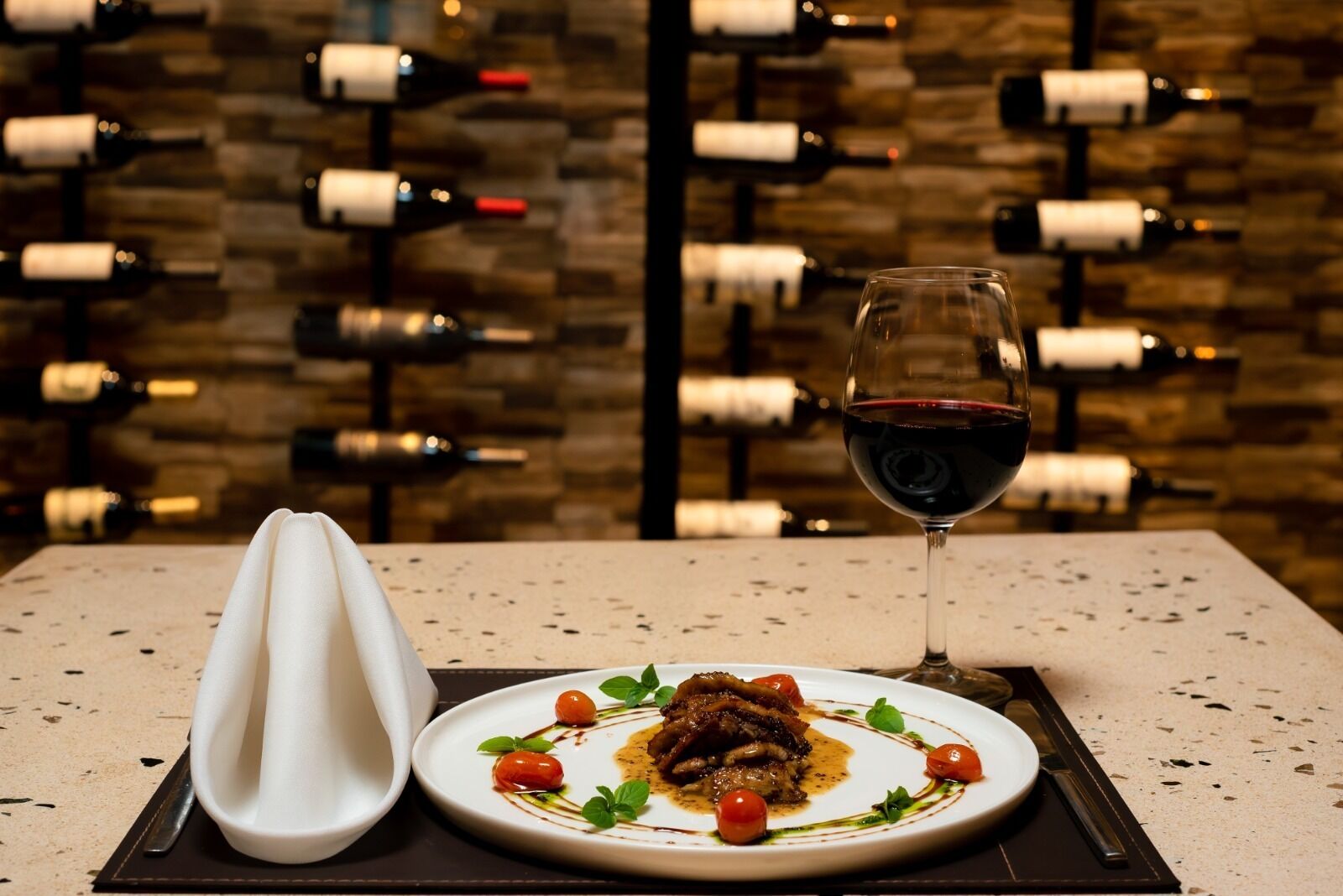 A dining table with a plate of food, a glass of red wine, and a white napkin.