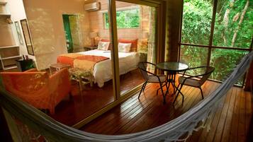 Una habitación con cama, una mesa, sillas, una hamaca y un ventanal con vistas a zonas verdes.