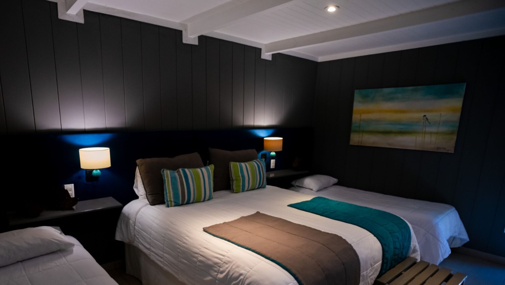 Een hotelkamer met een groot bed, twee bedlampen, een schilderij aan de muur en een houten bank.
