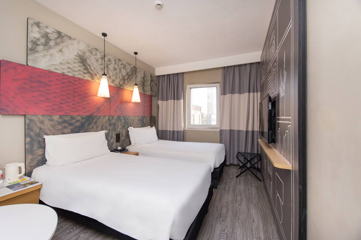 A hotel room with two beds, a TV, a coffee machine, and a window with curtains.