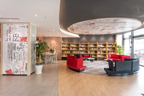 A modern library with red and black seating, wooden bookshelves, and a large circular ceiling feature. - ibis Shanghai Lianyang (Shanghai)
