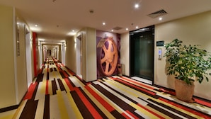 A hotel hallway with a striped carpet, a large wall mural, and an elevator. - ibis Xiamen Kaiyuan (Xiamen)