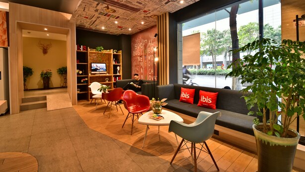 A modern interior with a sofa, red chairs, a coffee table, and a large window with a view of the street. - ibis Xiamen Kaiyuan (Xiamen)