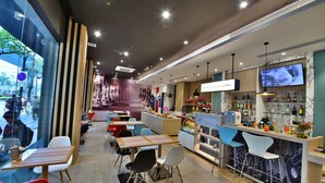 A modern cafe with tables and chairs, a bar area, and a TV screen. - ibis Xiamen Kaiyuan (Xiamen)