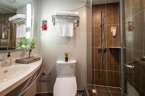 A modern bathroom with a white sink, a glass shower enclosure, and a toilet with a towel rack above it.